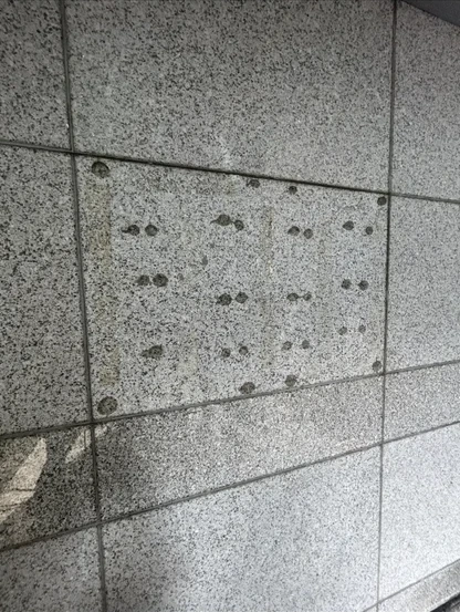 화강암 외벽 타일에 검은 실리콘·본드 잔여물이 점점이 남은 제거 전 현장