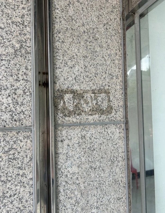 화강석 벽면에 필름·시트지 부착 자국이 사각형으로 남은 제거 전 현장